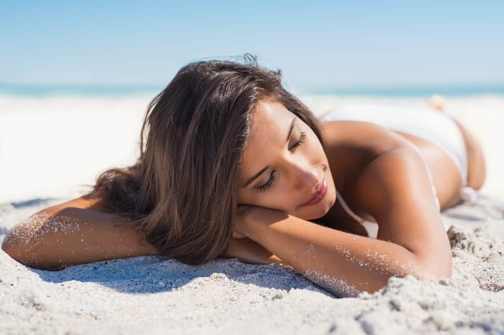 girl lying down under the sun tanning in a tropical beach