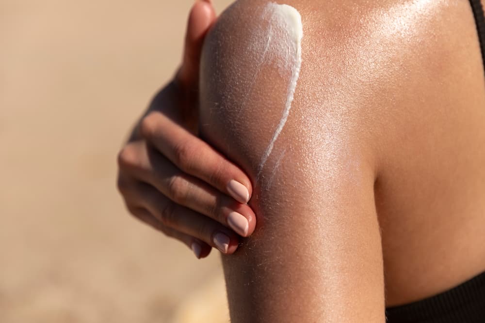 woman applying sun cream or sunscreen on her tanned shoulder