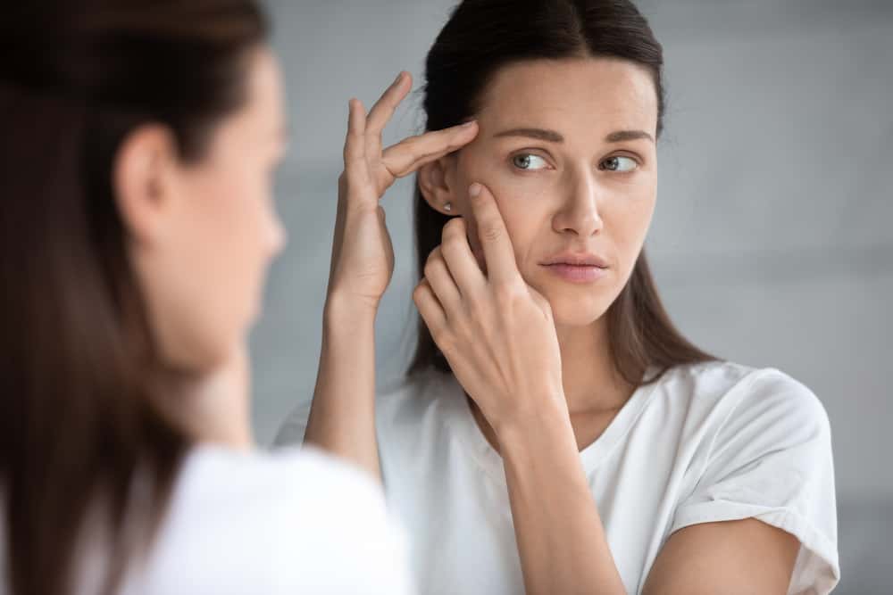 Anxious young woman look in the mirror worried about wrinkle or acne on unhealthy skin