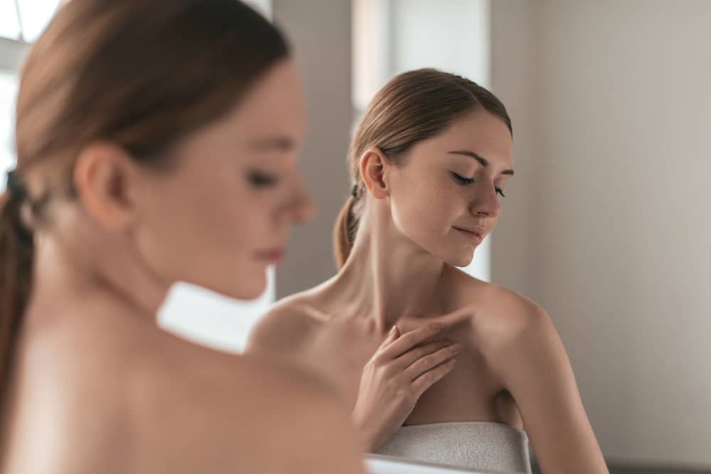 Over the shoulder view of young woman touching her skin