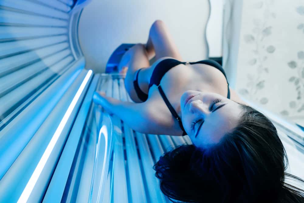 girl in a black swimsuit lies in a horizontal solarium